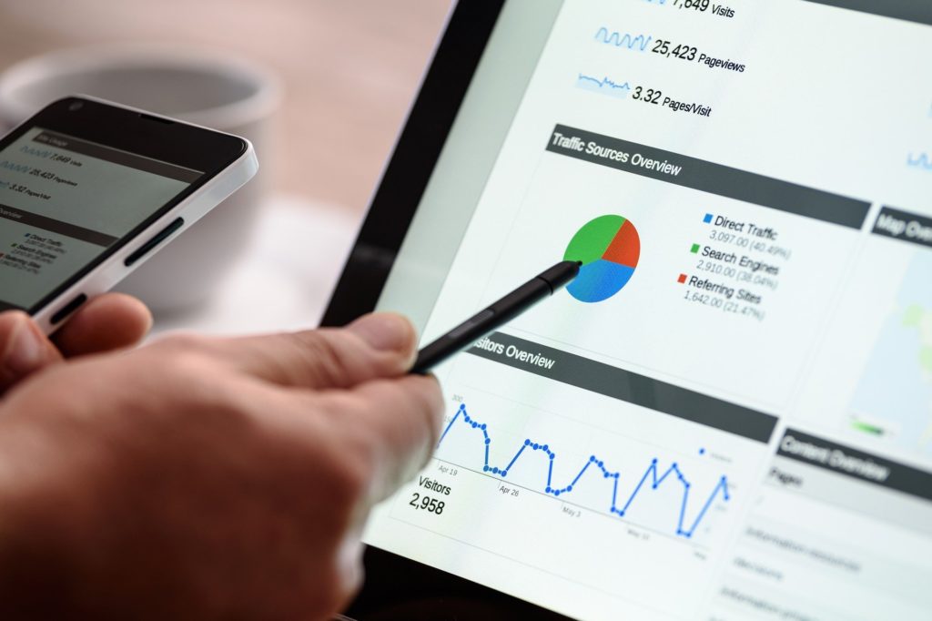 Foto eines Laptop-Bildschirms. der ein Dashboard einer Web-Analytics-Lösung zeigt, im Vordergrund eine Hand mit einem Stift